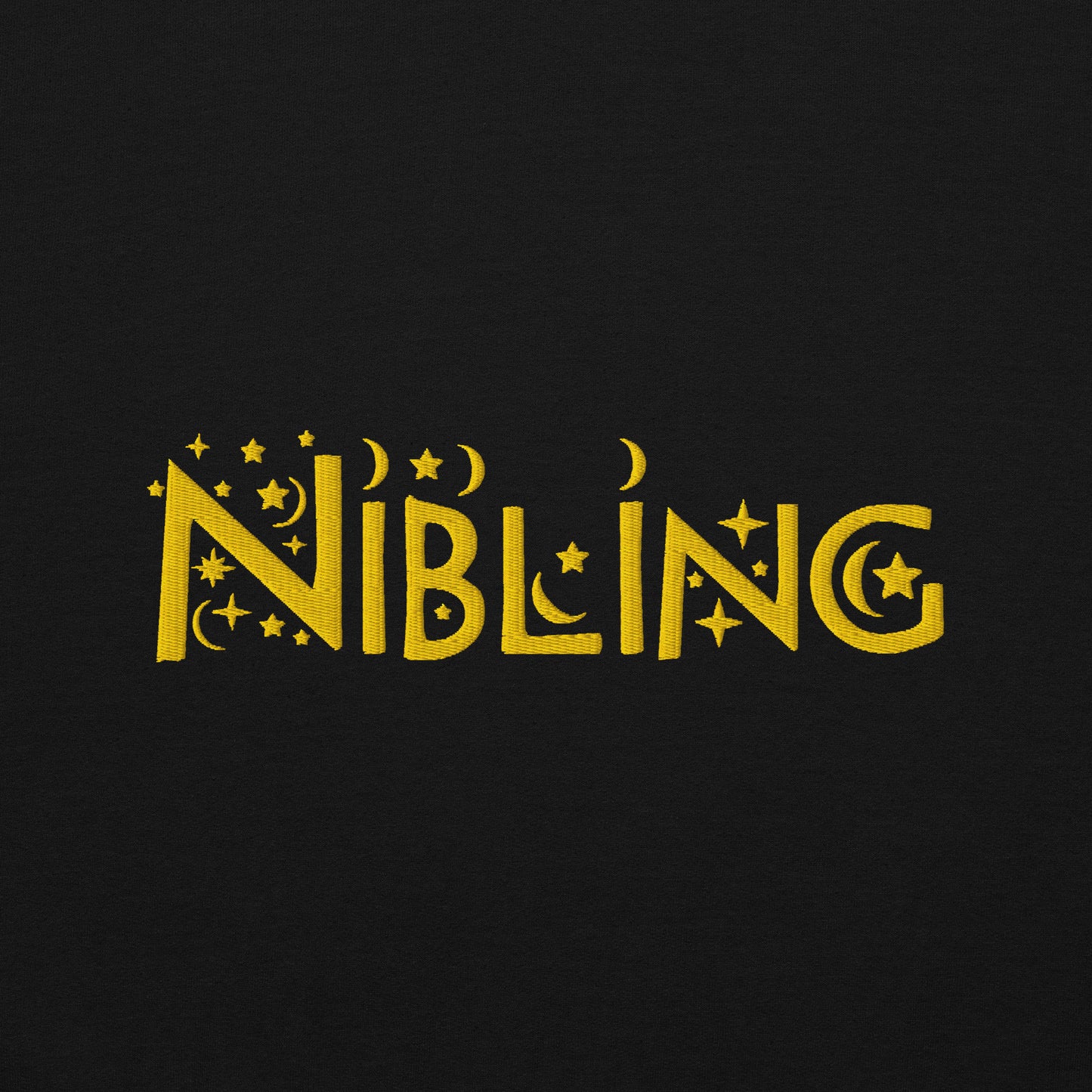 Close-up of “Nibling” embroidered in gold thread on soft black cotton fabric, featuring celestial motifs like stars and moons; gender-inclusive design by Galactic Flow
