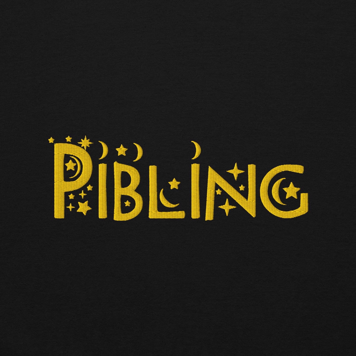 Close-up of “Pibling” embroidered in gold thread on soft black cotton fabric, featuring celestial motifs like stars and moons; gender-inclusive design by Galactic Flow