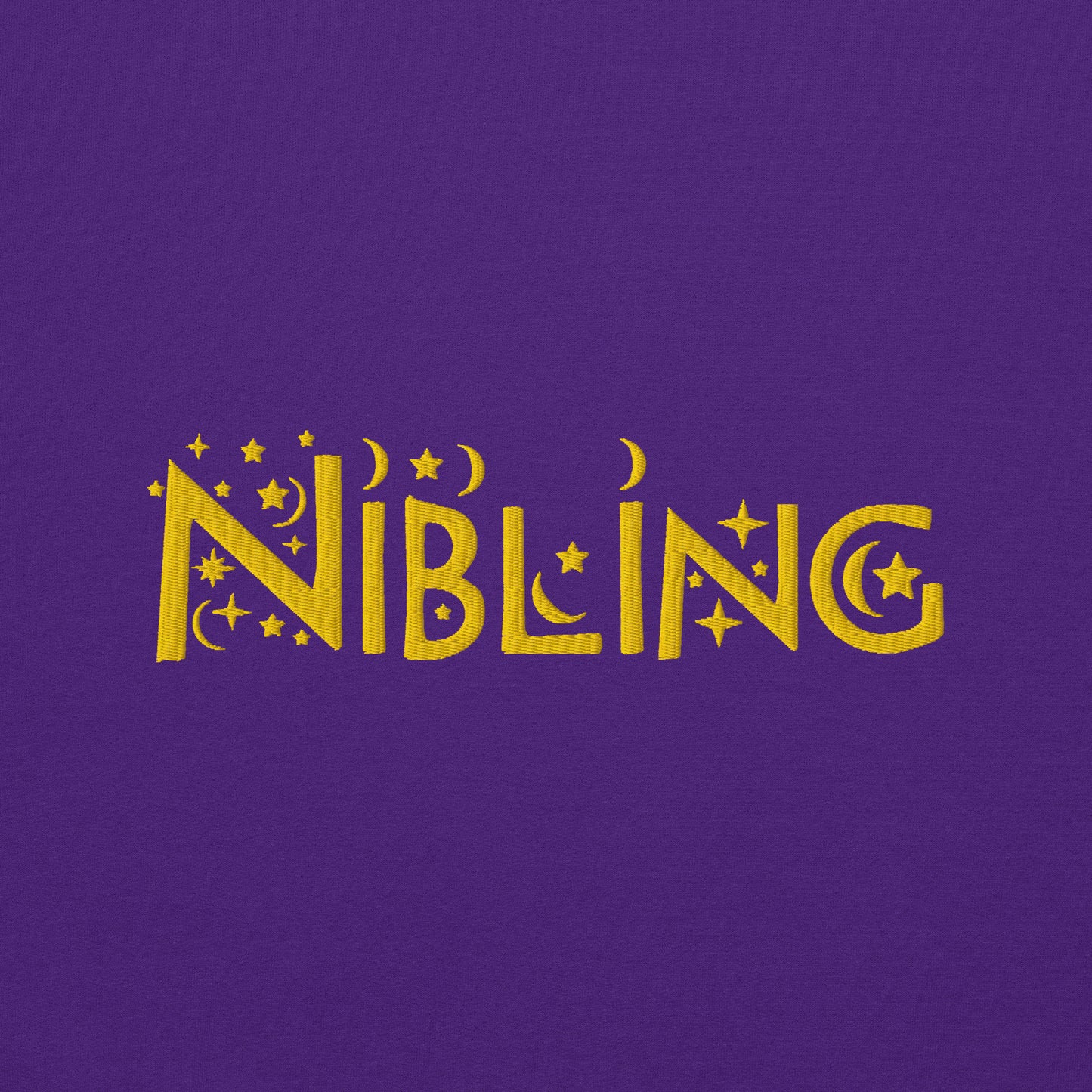 Close-up of “Nibling” embroidered in gold thread on soft purple cotton fabric, featuring celestial motifs like stars and moons; gender-inclusive design by Galactic Flow