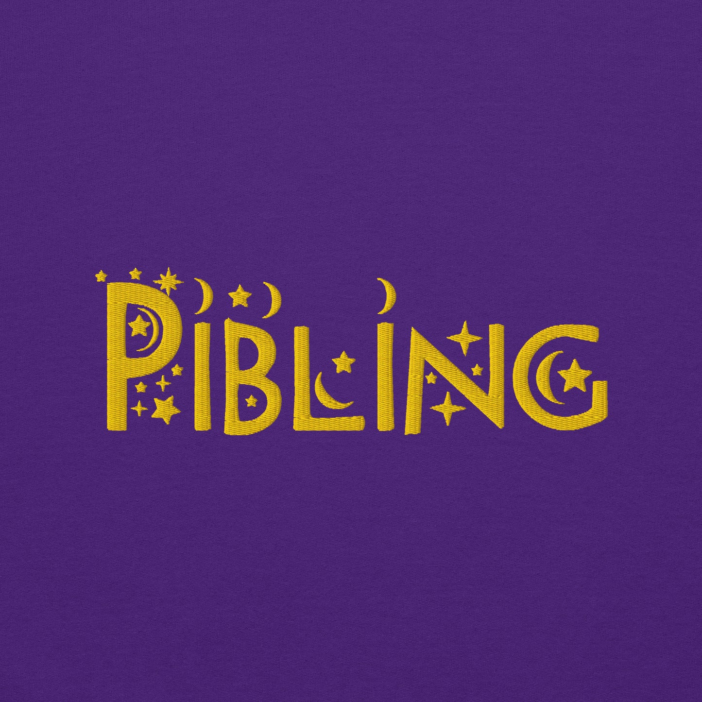 Close-up of “Pibling” embroidered in gold thread on soft purple cotton fabric, featuring celestial motifs like stars and moons; gender-inclusive design by Galactic Flow