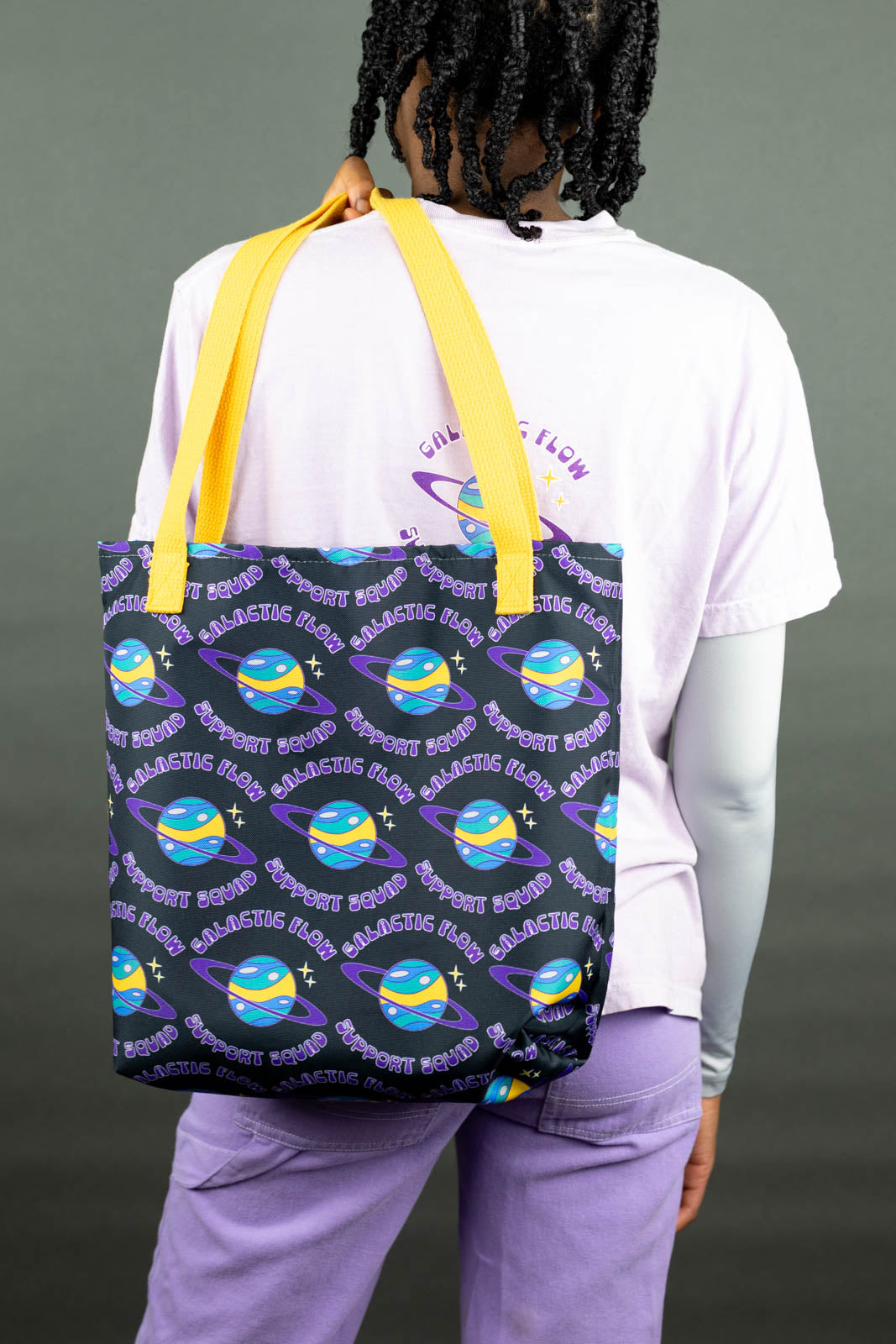 Kassidy wearing a black Support Squad Tote Bag with star pattern and yellow straps, on a gray background