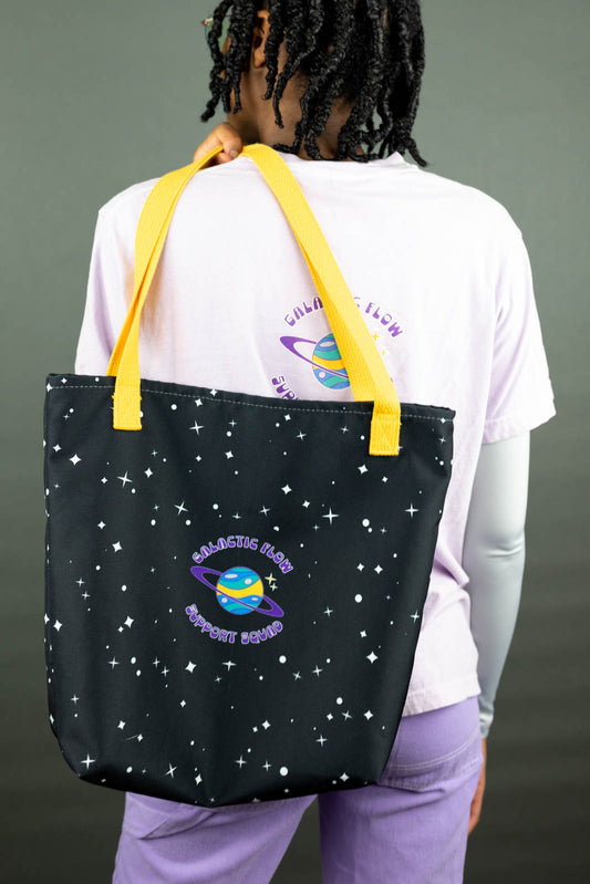 Kassidy wearing a black Support Squad Tote Bag with star pattern and yellow straps, on a gray background