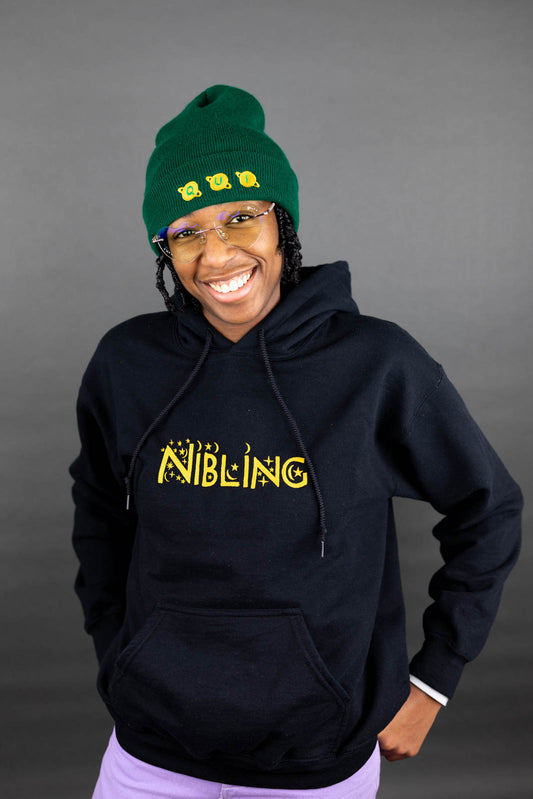 Person wearing a black hoodie with 'NIBLING' text, green beanie, and glasses on a gray background